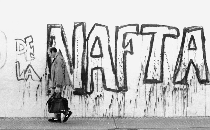 Man walks in front of a wall spray painted with "NAFTA"