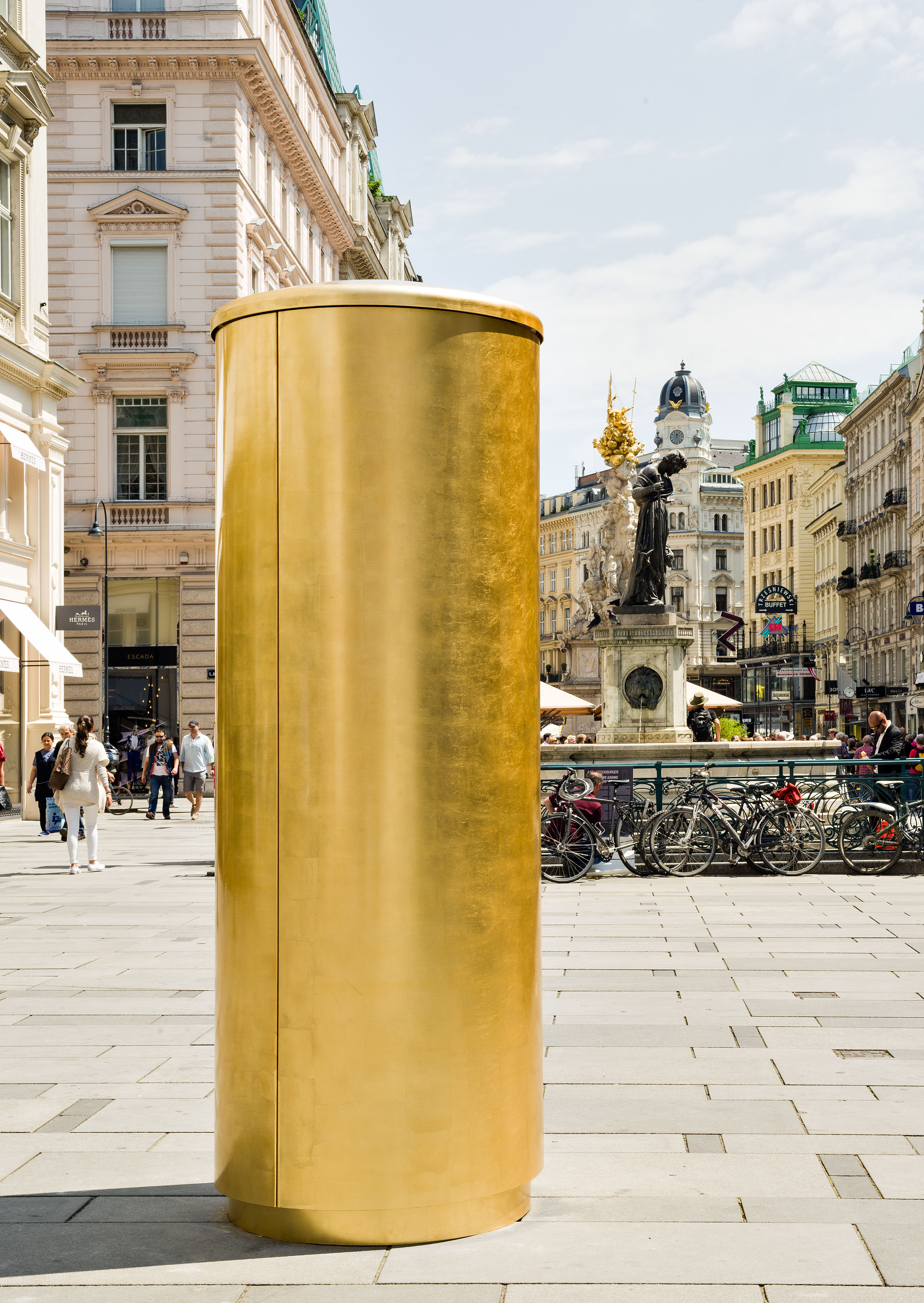 Golden cylindrical artwork in Italian city street.