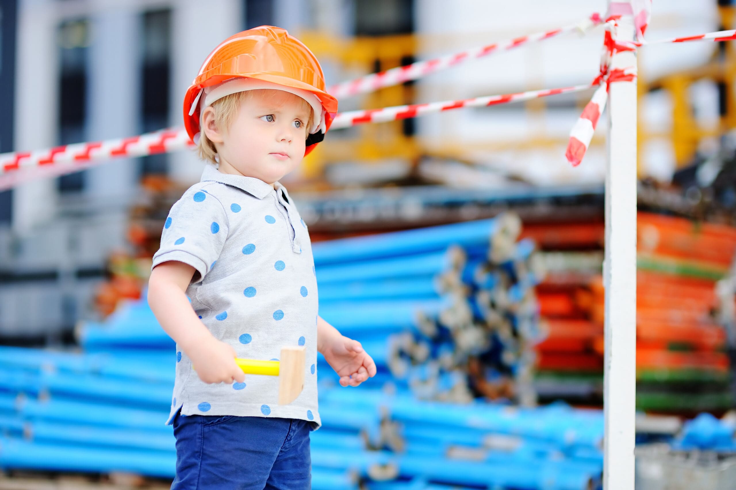 Portrait of serious little builder in hardhats with hammer working outdoors