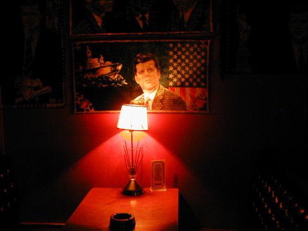 Picture of JFK on wall, a table underneath him with a red light