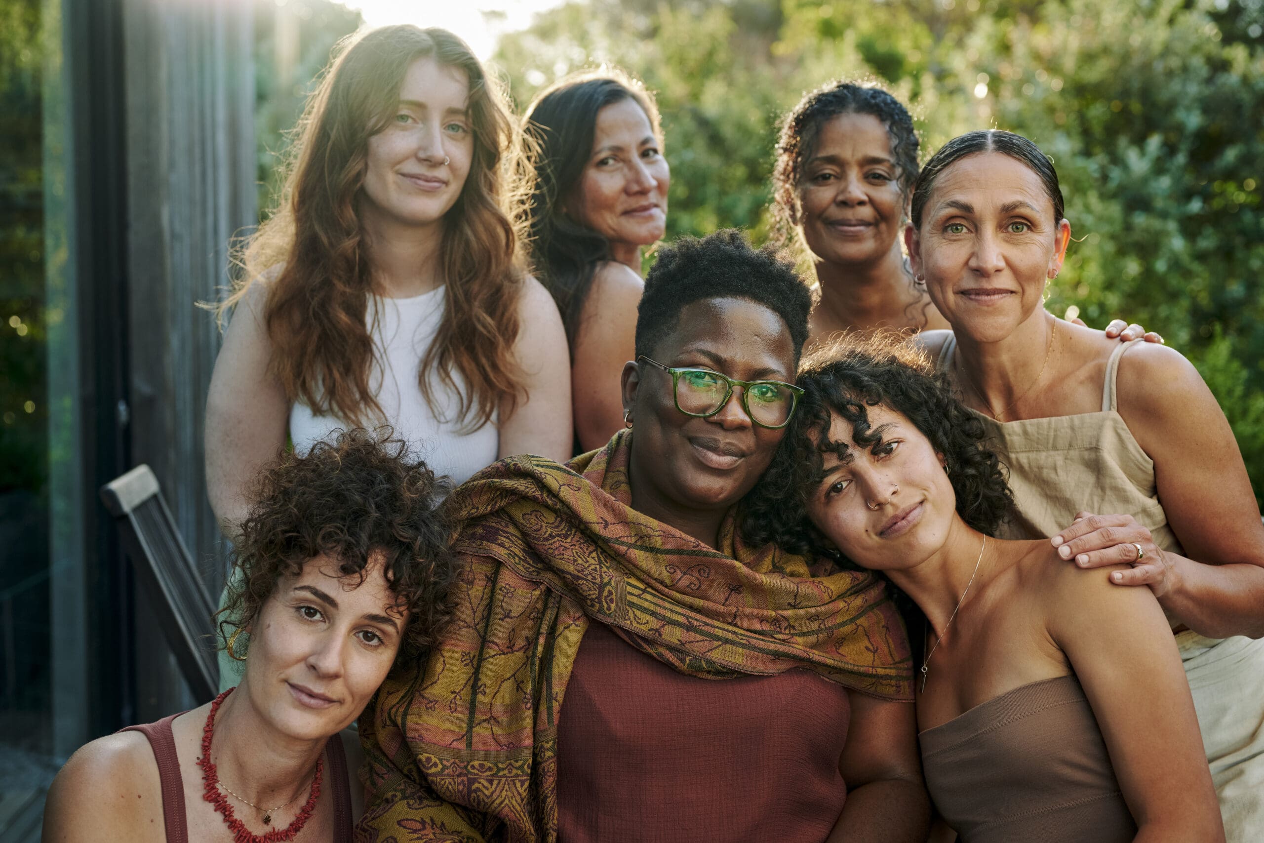 Portrait of a diverse group of supportive women smiling while sitting together outdoors on patio during a summer wellness retreat