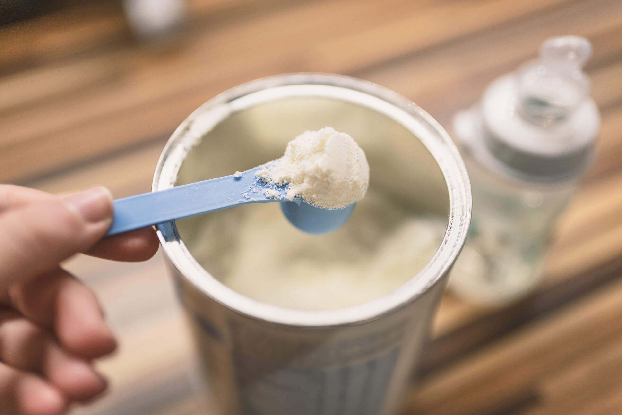 Milk powder for baby in measuring spoon on can. Powdered milk with spoon for baby. Baby Milk Formula and Baby Bottles. Baby milk formula on kitchen background