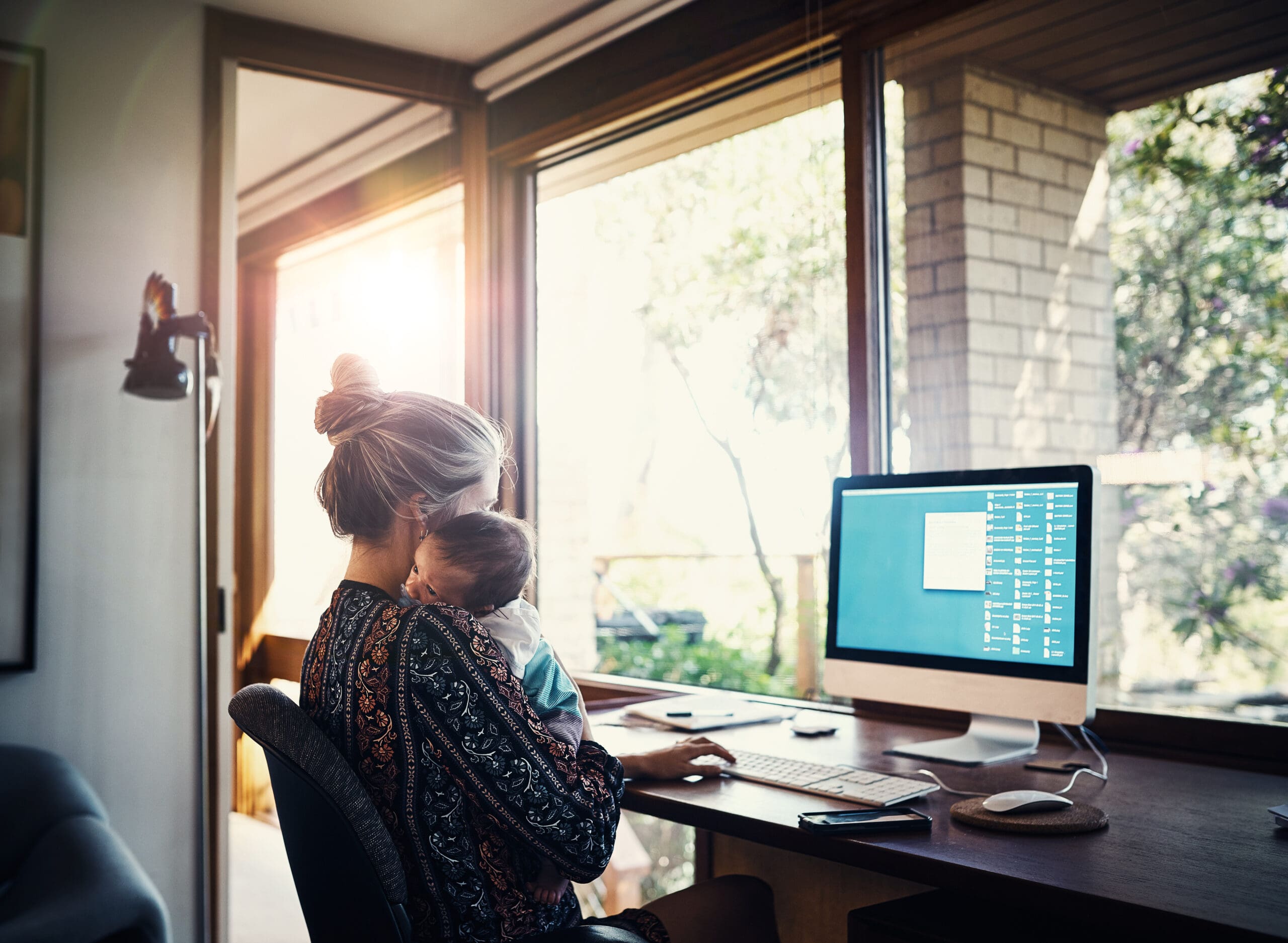 Shot of a young woman working at home while holding her newborn baby son