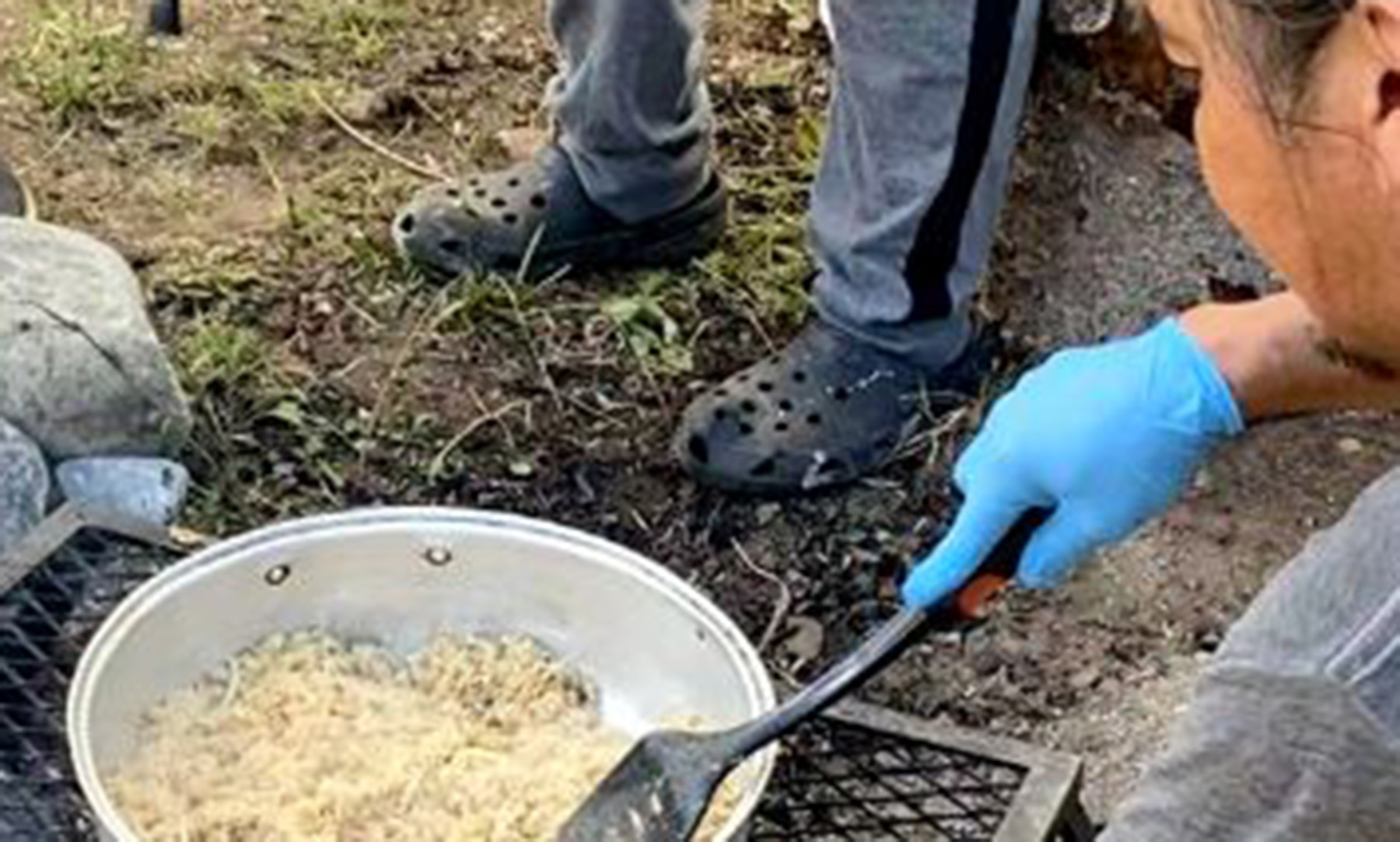 back view of someone cooking food on outdoors fire source