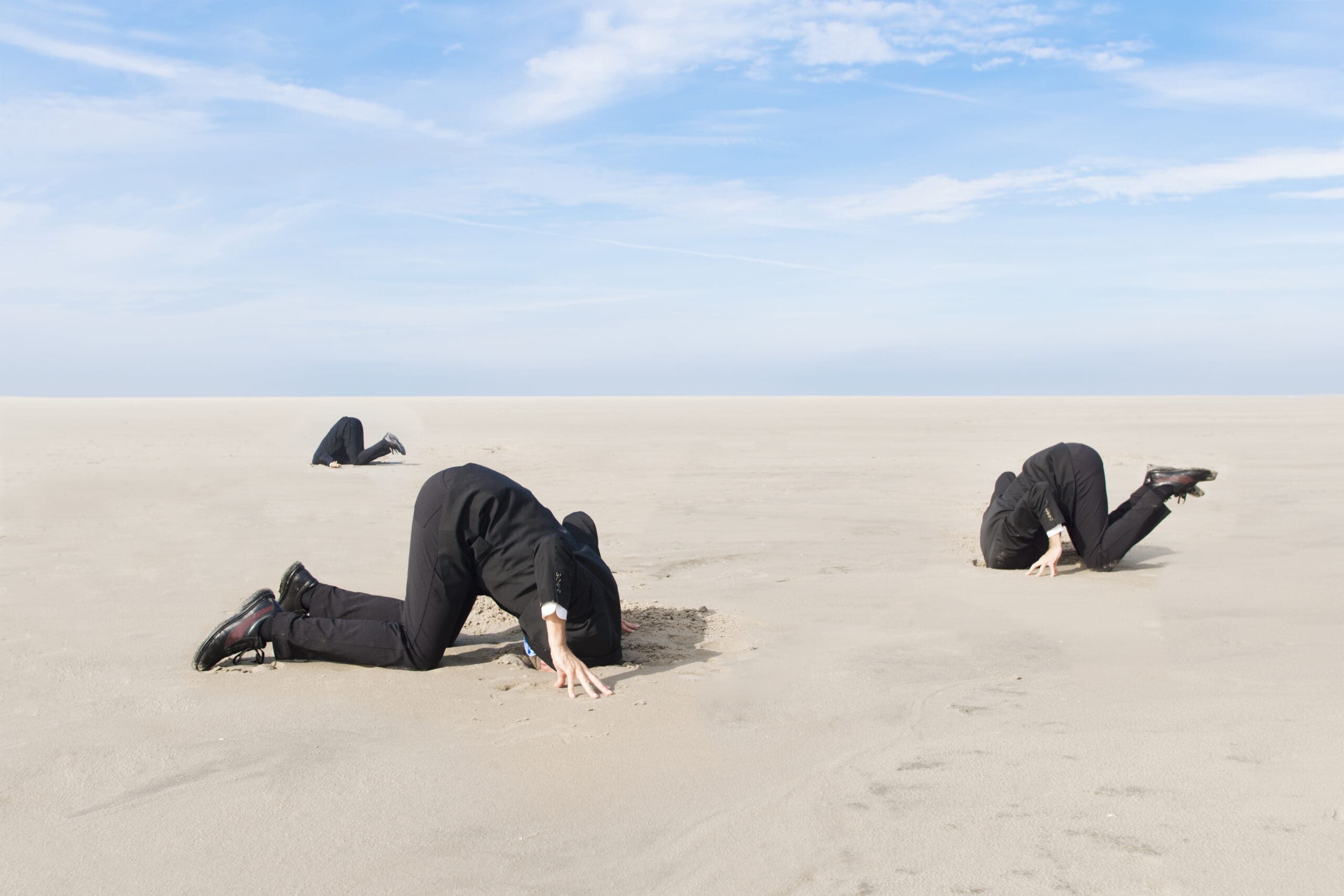 Three business men, hiding their heads in the sand.